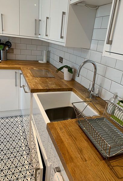 A tidy kitchen with a wooden worktop, a butler sink and white cupboards