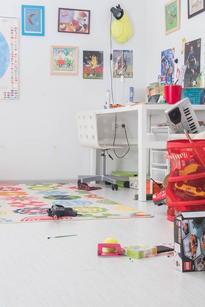 A bright child's bedroom with a desk, a rug and red toy storage