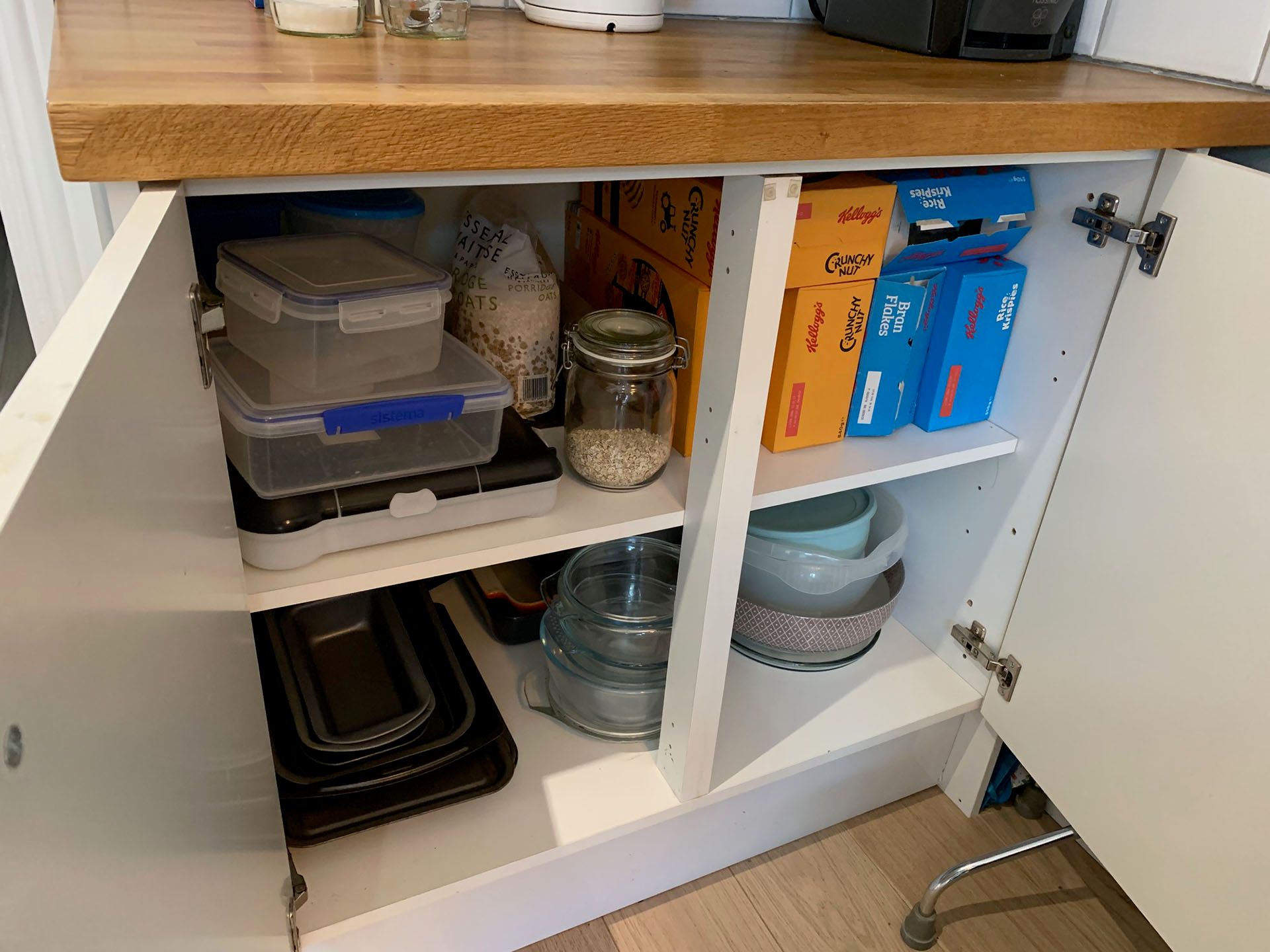 An open kitchen cupboard with food in clear containers and cereal boxes lined up on the shelves
