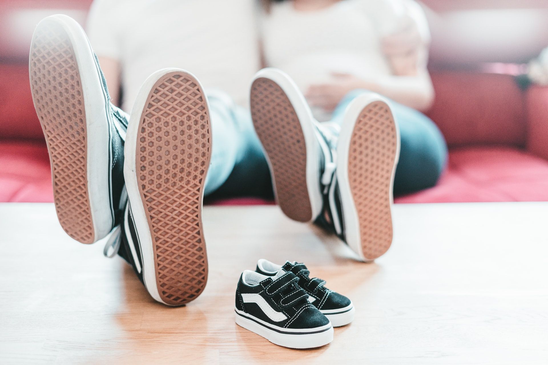 Two pairs of adult trainers with their feet up on a table beside a tiny pair of baby trainers