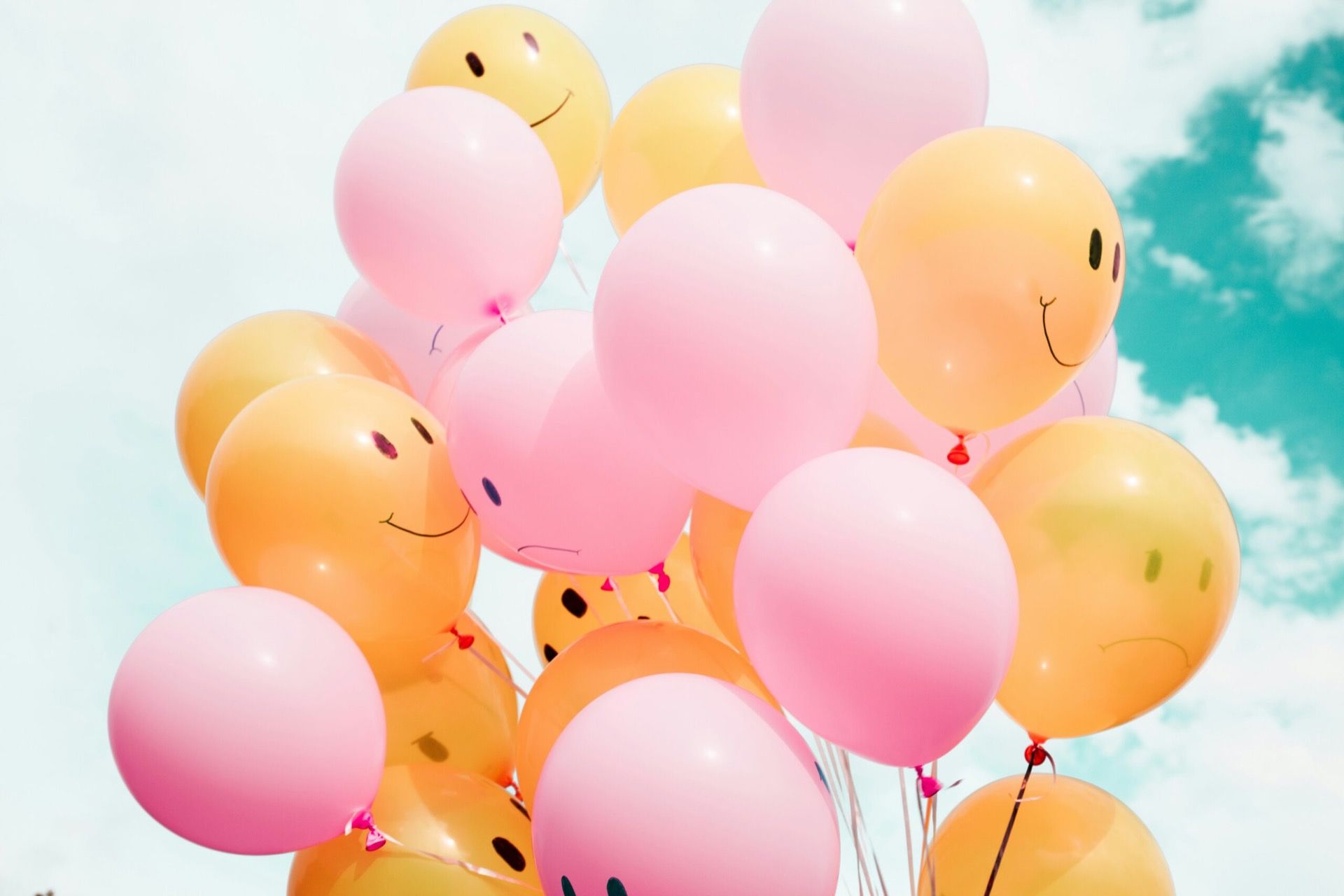 A bunch of pink and yellow balloons with smiley faces against a blue sky