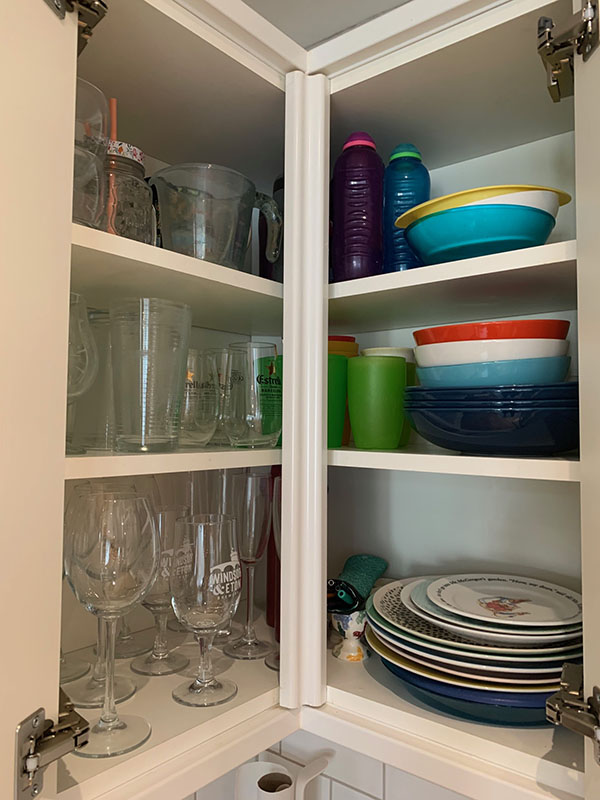 A kitchen cupboard with organised glassware by type, plates and bowls, as well as drinking bottles