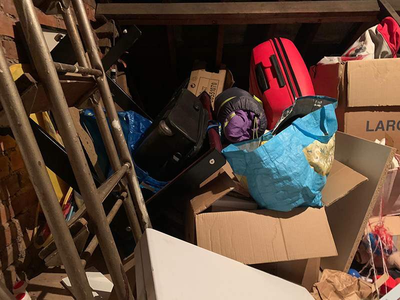 Original loft area, everything is piled on the floor, with boxes and items haphazardly strewn around. There is no space to walk across the space to reach anything at the far wall